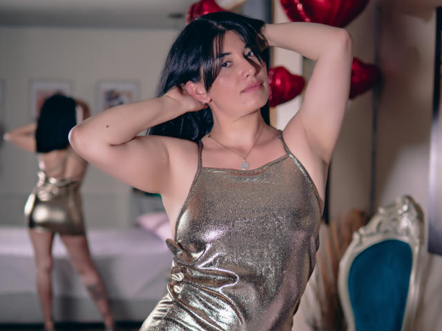 DianaMaris with black hair, wearing a shiny gold dress, arms up, looking at camera, showing her tits, reflection in mirror, red heart balloons in background.
