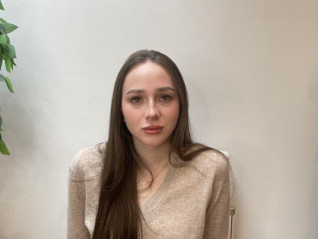 LindaGarner has long brown hair, pale skin, and is wearing a beige sweater. Her tits are small, and she has a cute, slightly serious face with pink lips.