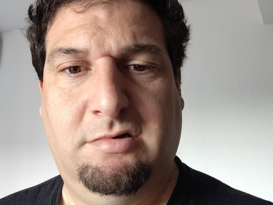 Jmmich has a chubby face with light skin, brown eyes, short curly black hair, and a stubble goatee. He's wearing a black shirt and looking slightly confused.