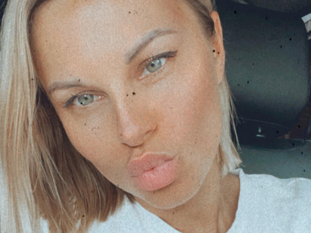 BelleLisaG's pouty face, blonde hair, green eyes, and freckles are in a selfie with slightly parted lips and a white shirt. Her nose is small and her lips are plump.