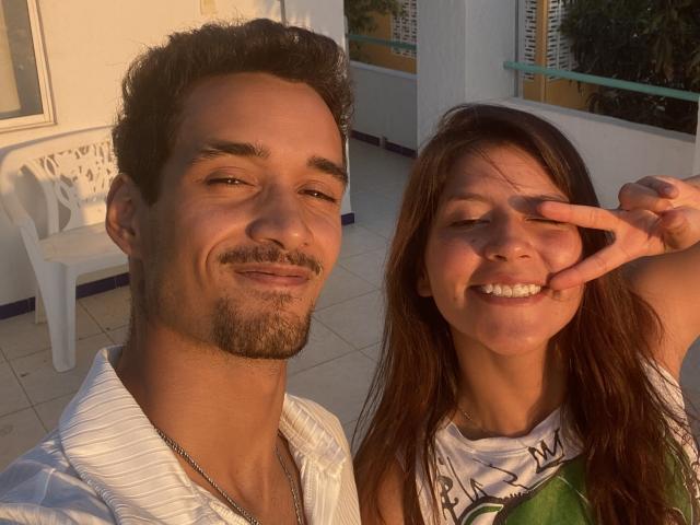 LailaAsher, con cabello castaño rizado corto, ligera barba, camisa blanca, sonriendo a la cámara. LailaAsher, con cabello castaño largo, sonriendo, haciendo el gesto de la paz, vistiendo una camisa verde y blanca..