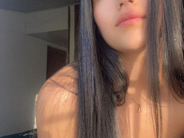 IssaPuasini's face, showing her pouty pink lips, long straight black hair, and tan skin, with a small gold necklace visible, and sunlight casting a warm glow.