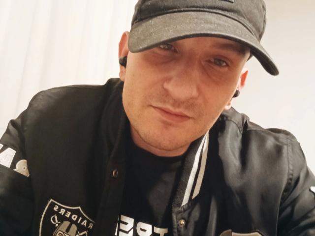 Une MilfAnaLyzer corpulente, sexy, avec une casquette noire, une veste noire et des écouteurs, qui a l'air légèrement agacée, porte un t-shirt noir et des rayures blanches sur la veste..