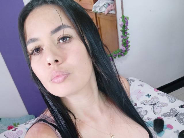 AshleyKatelyn ha lunghi capelli neri, occhi marroni e labbra rosa. Indossa una maglietta con un motivo a farfalle, che lascia intravedere leggermente il seno. Sta guardando la fotocamera con un'espressione accigliata..
