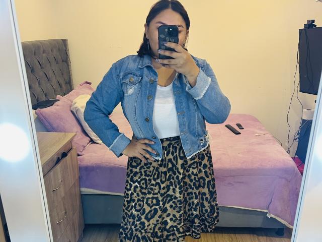 KarlaWild in a denim jacket, white top, and leopard print skirt, taking a mirror selfie with a phone, showing off her ass in the reflection.