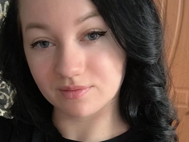 RikkiTTikki ha la pelle chiara, l'eyeliner nero e i capelli neri ondulati. Sorride, mostrando le labbra rosa, gli occhi azzurri e un viso leggermente arrossato. Sullo sfondo, una porta di legno..