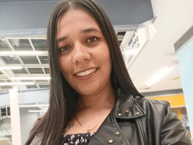 PauletteLoveX has long black hair, brown eyes, and a cute smile. She's wearing a black leather jacket with gold buttons and a floral top, showing a small tattoo.