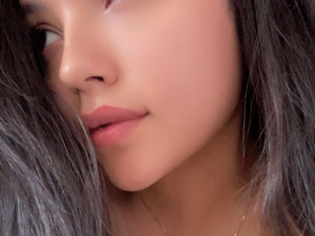 IssaPuasini's face, focusing on her smooth, tan skin, full pink lips, and dark, wavy hair. Her nose is slightly upturned, and she's looking to the side.