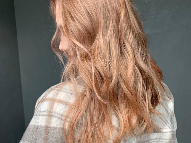 HotCaramells has wavy, blonde hair with pinkish-brown highlights, wearing a grey plaid shirt. Her face is in profile, smiling softly.
