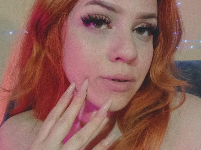 SpicyGrace ha i capelli arancioni, labbra piene e rosa, e lunghe ciglia. Toccata il mento con le dita delle mani, curate di rosa. La sua espressione è leggermente accigliata. Il suo seno non è visibile..