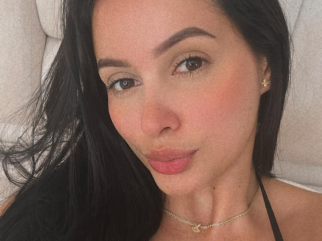 EmilyParkerr with pouty lips, black hair, brown eyes, light skin, small nose, subtle makeup, gold necklace, small earrings, and slightly flushed cheeks, looking directly at the camera.