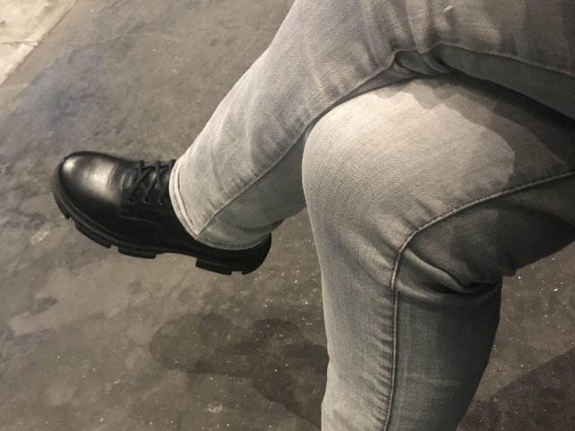 MoonBlossom draagt een lichtgrijze, licht versleten broek. Ze heeft zwarte, glanzende veterschoenen met dikke zolen aan. Eén been is over het andere gekruist..