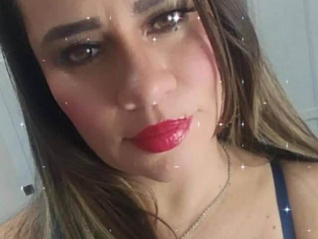 CharllotI has pink blush, red lipstick, and brown eyes with long lashes, wearing a blue strap top, with brown hair and a subtle smile, and a small boogers on nose.