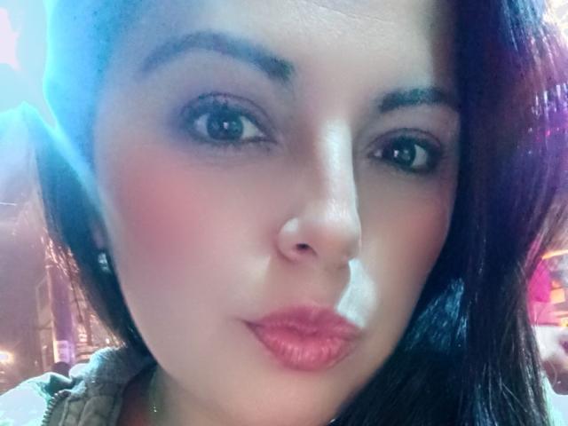 Seher's face with pouty pink lips, dark eyebrows, and slightly flushed cheeks. She has dark brown hair, green eyes, and a light skin tone with a subtle glow.