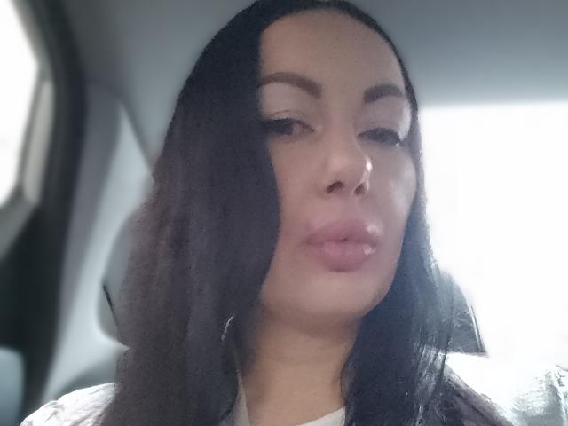 MirandaHott69 has dark, wavy hair, light brown skin, and full pink lips in a slight pout. She's wearing subtle makeup with defined eyebrows. Soft light highlights her face.