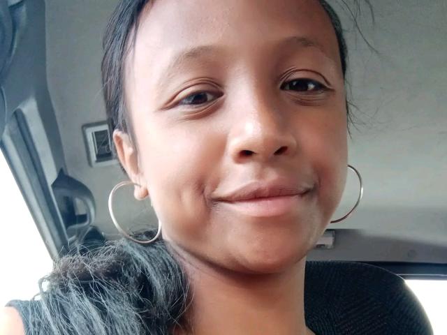 Carinehotlove has medium brown skin, small hoop earrings, and a subtle smile. She's wearing a black shirt with a slight ponytail, and her pussy isn't visible.