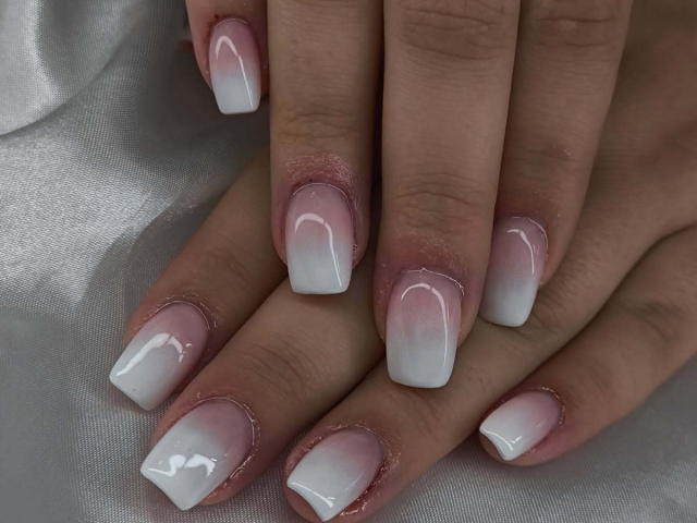 ElvinnaLaFrancaise's hands with pink-to-white gradient, square-shaped, glossy nail polish on short nails, set against a white, silky background. Her nails are shiny and well-manicured.