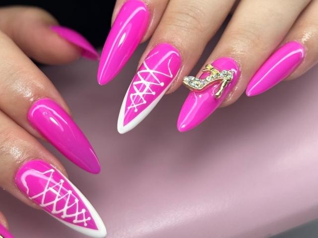 ElvinnaLaFrancaise's pink acrylic nails with white lace patterns, featuring a gold high heel ring with diamonds on the ring finger, have super long, sharp, glossy tips.