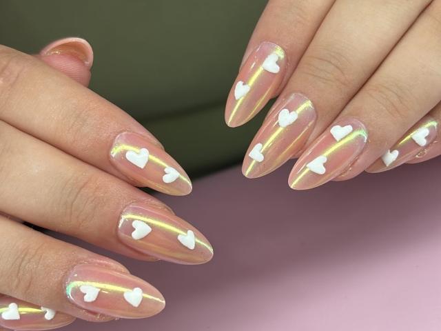 ElvinnaLaFrancaise's nails are glossy with a clear base, white heart decals, and rainbow reflections. Her hands are positioned with fingers slightly apart, showing off her stylish manicure.
