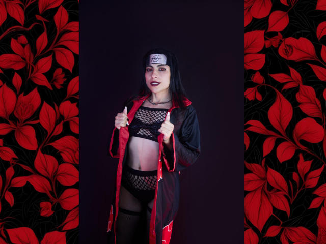 SamantaKi in black fishnet lingerie, red robe, and ninja headband, showing off her tits and pussy with dark lipstick, against red floral-patterned walls.