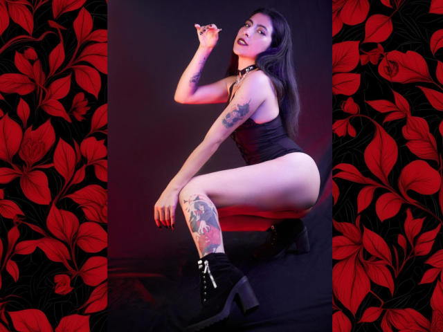 SamantaKi with tattoos, squatting, wearing a black corset, high-heeled boots, holding a cigarette, black choker, showing her ass and thigh tattoo, dark red lighting.