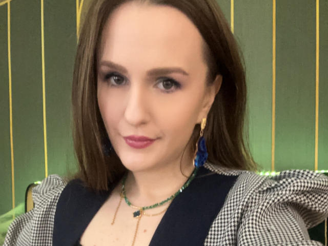 VanessaBeauty has light skin, brown hair, and blue eyes. She's wearing a checkered top, green necklace, and blue earrings. Her pink lips and subtle makeup are sexy.