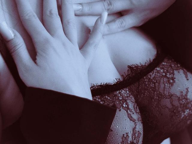 LilithBlondy's handen omvatten zachtjes haar blote borsten, bedekt met zwarte kant, terwijl haar vingers nagels tonen die zijn gemanicuurd. Monochromatische blauwe tint..