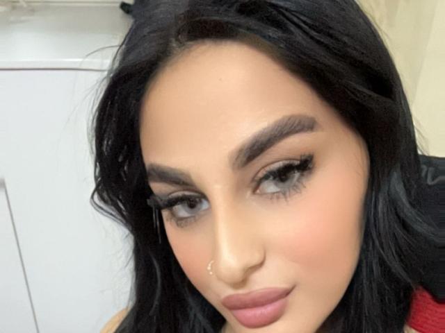 SophyAngels ha i capelli scuri e ondulati, sopracciglia folte, ciglia lunghe, un piercing al naso e labbra rosa. La sua pelle è marrone chiaro e guarda leggermente di lato..