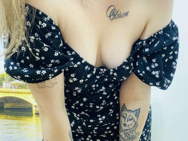 KarKutie has a tattooed chest and arms with a fox on her right and flowers on her left, wearing a black off-shoulder floral dress, showing her tits.