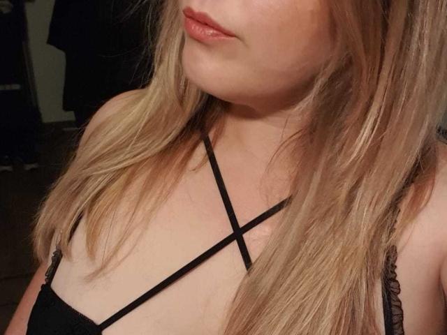 O rosto de Guimso, com cabelo castanho claro, lábios rosados levemente entreabertos, vestindo uma blusa preta com alças finas, mostrando o colo. Sua pele é clara e ela tem um olhar sutil e sexy..