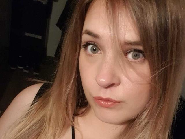 El rostro de Guimso, con cabello castaño claro y liso, ojos azules y un ligero puchero, vestida con una blusa negra, mostrando una piel clara y un maquillaje sutil, mirando directamente a la cámara..