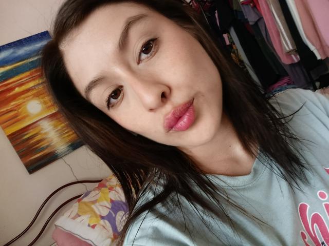 IsabellaPalacio with pouty pink lips, brown eyes, and straight brown hair, wearing a light blue shirt, looking at the camera. Boobs not visible, pussy not visible, ass not visible.