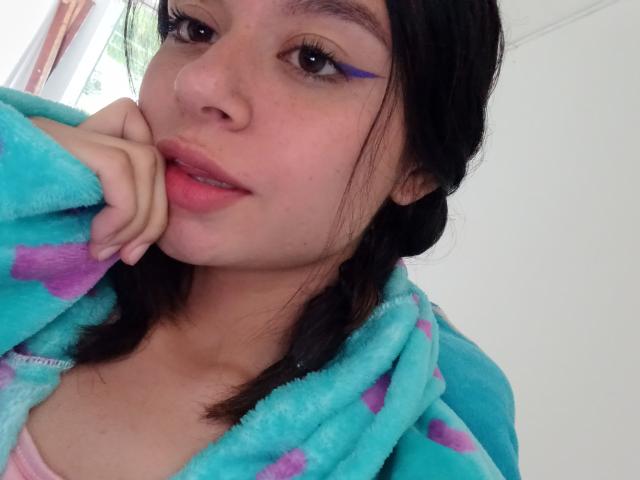 KennyAndLucy with blue eyeliner, pink lips, and hand on chin, wearing a teal and purple fuzzy robe, has a cute face and dark hair, in a selfie.