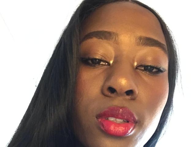 VioletGraice has glossy, shiny brown skin, long straight black hair, golden eyeshadow, thick black eyebrows, and bright pink glossy lips with a slight pout.