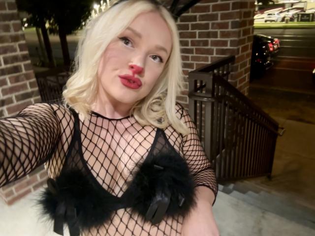 Cherry7up has blonde hair, red lipstick, and is wearing a black fishnet top with fluffy black accents covering her tits. She's taking a selfie outdoors at night.