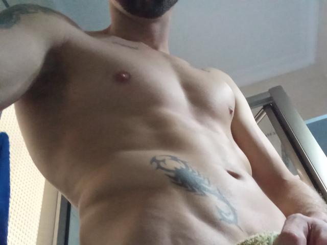 BeSilvioS' shirtless upper body, showing a tattoo on the right side of his torso, a trimmed beard, and a muscular, toned chest with small, hard nipples.