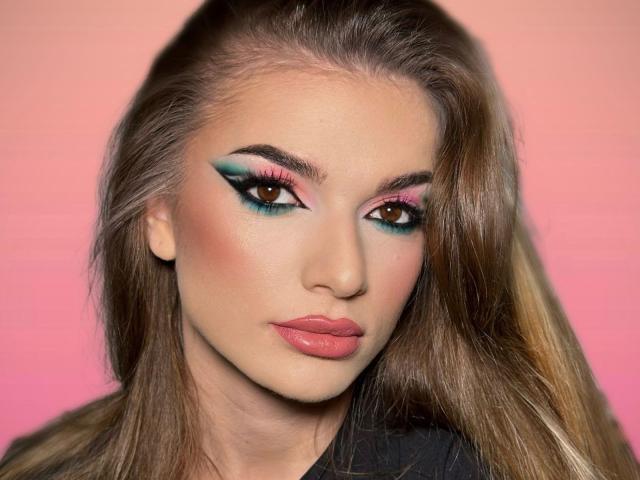 IngridI has shiny brown hair, pink glossy lips, and teal-green winged eyeliner with pink and blue accents. Her brown eyes are half-open and she's looking directly at the camera.