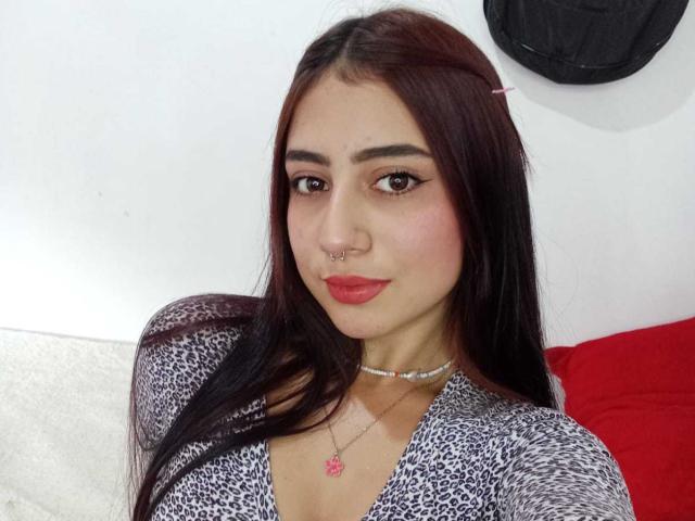SarahLark ha i capelli castano scuro, rossetto rosso, un piercing al naso e una maglietta a stampa leopardo, che lascia intravedere leggermente il seno in un selfie. Indossa una collana con un pendente rosa..
