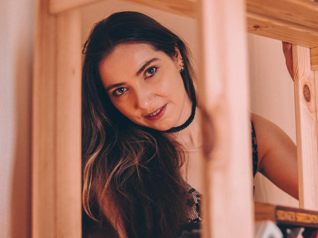 Decadance ha lunghi capelli castani, occhi azzurri e indossa un choker nero con una maglietta nera in pizzo, che spunta da una cornice di legno con un sorriso appena accennato..