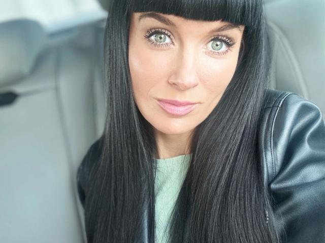 Minnieme-hot has straight black hair, green eyes, and pink lipstick. She's wearing a black leather jacket over a green top. Her ass is not visible.