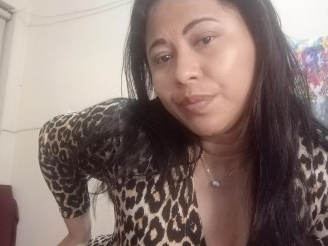 MiaSalomeChaude with black hair, wearing a leopard print top, slightly pouty lips, and a necklace, leaning forward, showing her tits. Soft lighting, casual selfie.