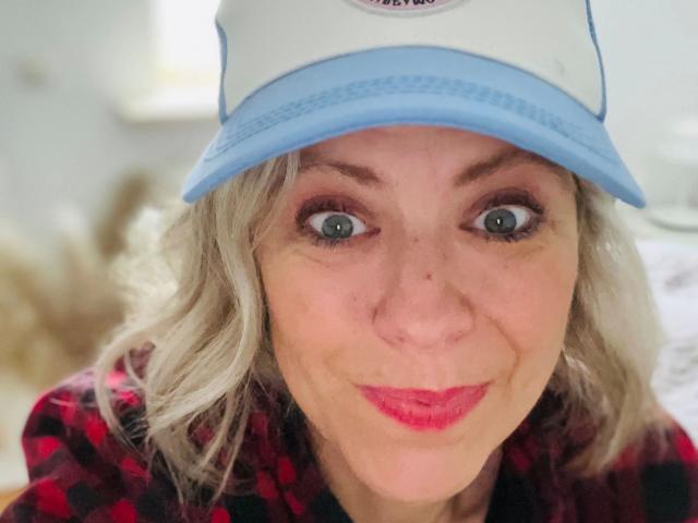 MiaHase-hot with blue eyes, pink lipstick, wavy gray hair, and a white cap with a blue brim, wearing a red and black checkered shirt, smiling at the camera.