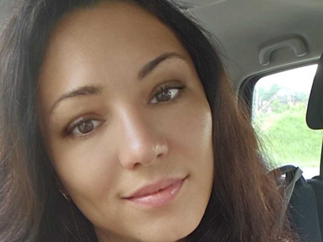 AmelyBrown's face, brown eyes, subtle smile, medium brown skin, small nose ring, long dark brown hair, light pink lips, inside a car, looking at the camera.