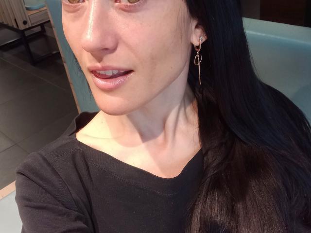 BellaJulls has shiny, pale skin with slight redness, long black hair, and is wearing a black top with a small, shiny lip color. She has a small, delicate earring.