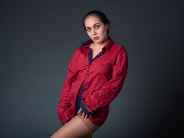 IziPaterson with red button-up shirt, blue underwear, hands in pockets, looking at camera, dark background, serious expression, slightly leaning forward, red lipstick, dark hair, pale skin.