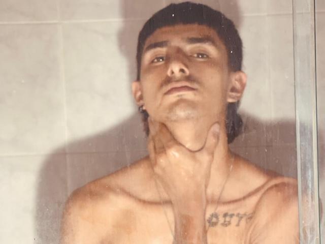 NathanMaxime, avec ses cheveux noirs courts, sa peau brune et un tatouage sur sa poitrine, se tient sous la douche, torse nu, une main agrippant son cou. De l'eau sur le verre..