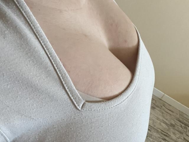 Rimia's tits are showing through a low-cut, white, sleeveless top, with her pale skin and slight breast cleavage visible. The fabric has a subtle texture.