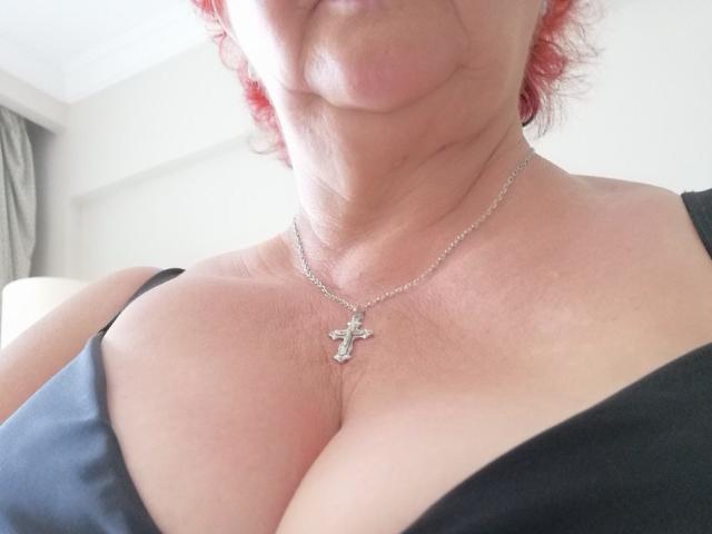 PeggySoft's chest with large boobs, wearing a black bra, silver cross necklace, and red curly hair, shown from neck to cleavage.