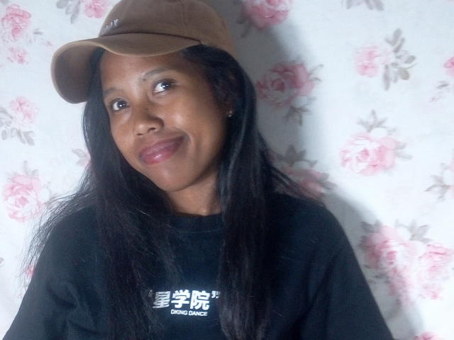 KattyMiriam has dark brown skin, long black hair, and is smiling with pink lips. She's wearing a brown cap and a black shirt, looking cute.
