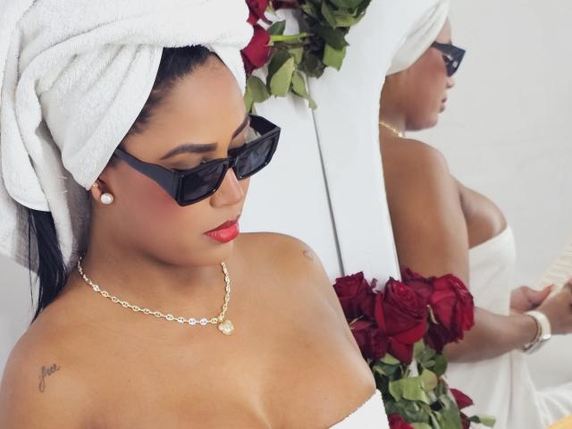 BarbaraKano with a white towel on her head, black sunglasses, red lipstick, pearl earrings, and a necklace, holding red roses, showing her bare tits in a mirror reflection.